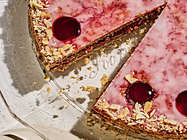 Kuchen mit rosa Glasur und Kirschgarnitur auf einer Glasplatte, Stueck herausgeschnitten.