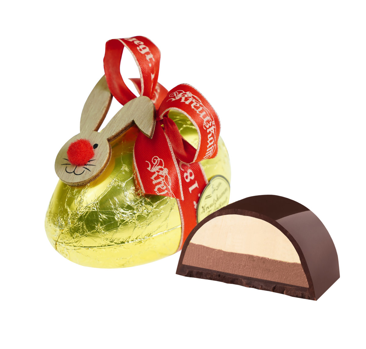 Nougatei-Gold-Anschnitt Ein Schokoladenei mit Holzhasenkopf und rotem Band (Text: "Backhaus Kreutzkamm"), neben einer aufgeschnittenen Praline, auf wei