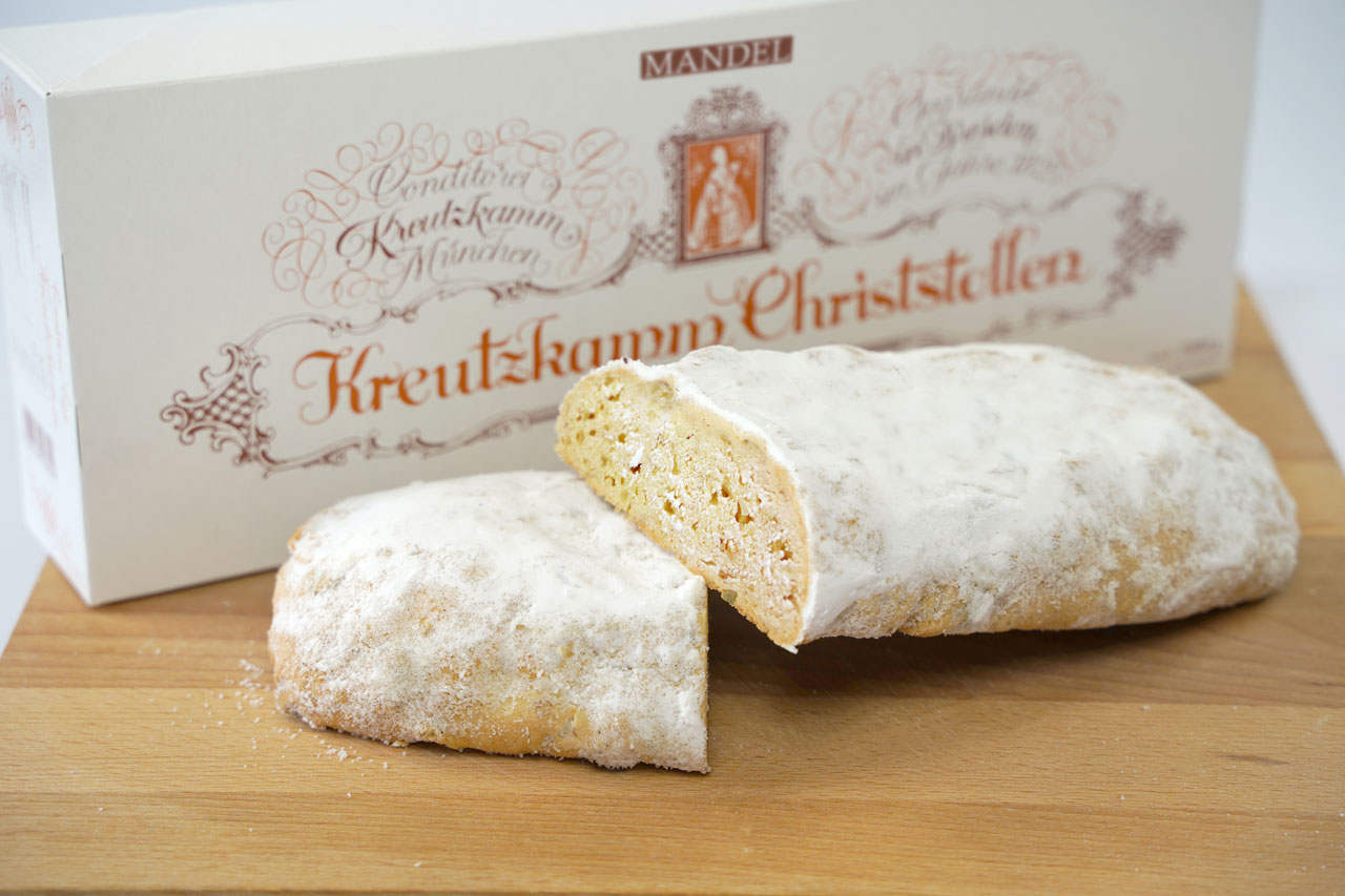 04-Mandelstollen Ein halbierter Christstollen liegt auf einem Holzbrett vor einer Schachtel mit der Aufschrift: "Kreutzkamm Christstollen Mandel."