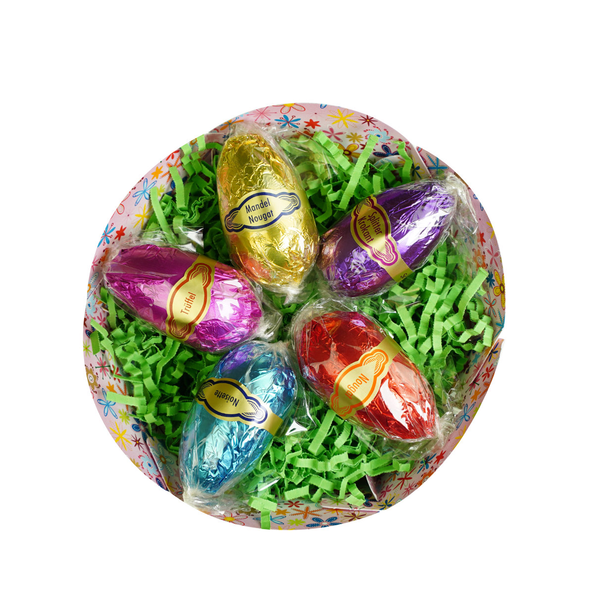 Dessert-Ei-5-st-02-Netz Bunte Schokoeier in Folie verpackt liegen auf gruenem Ostergras in einer verzierten Schale. Text: Mandelnougat, Vollmilchtrueffel, Nougat, Tuertel, Haselnuss.