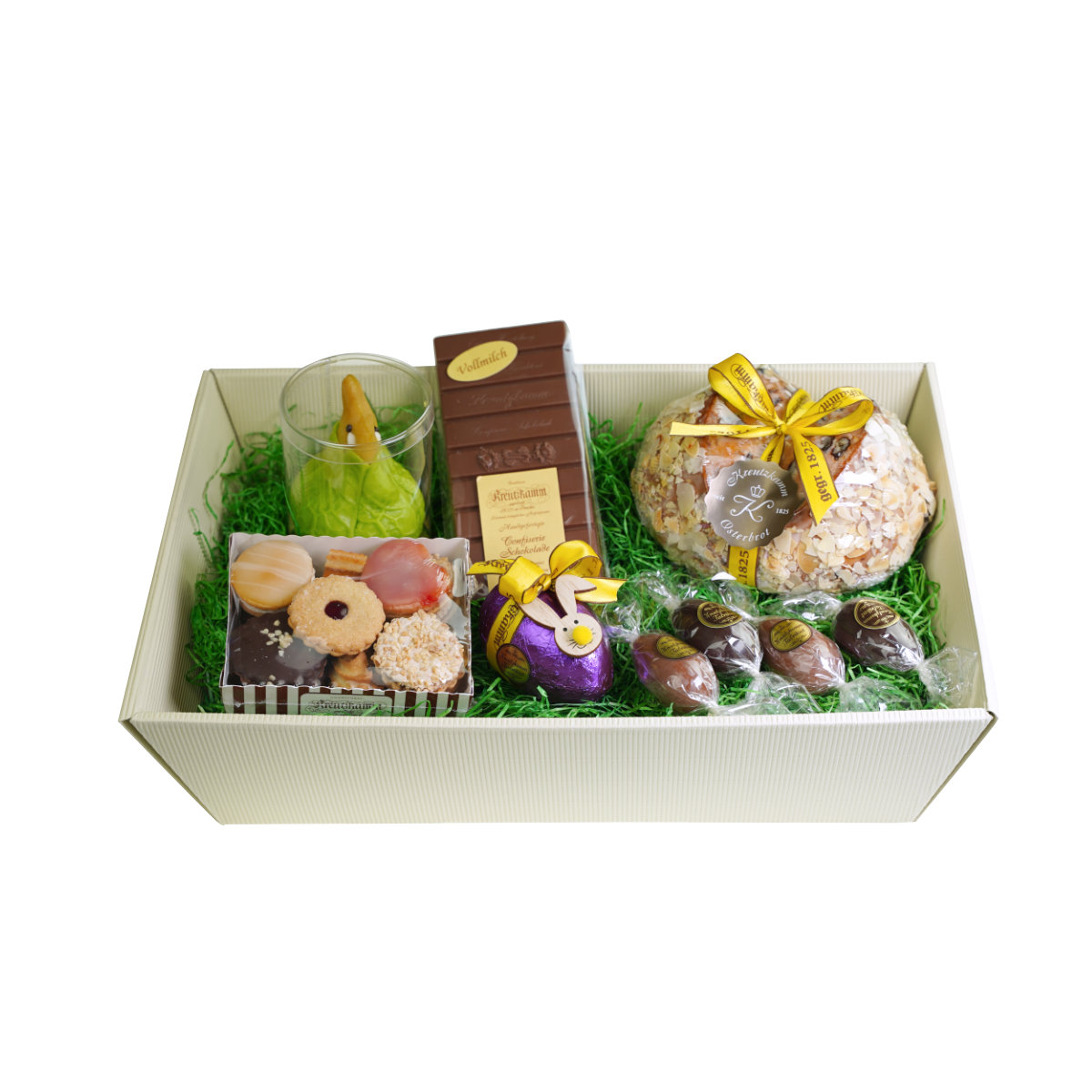 Osterpaket-Nr-02 Geschenkkorb mit verschiedenen Suessigkeiten wie Keksen, Schokolade, Brot und Pralinen auf gruenem Papier. Text: Backhaus Kreutzkamm.
