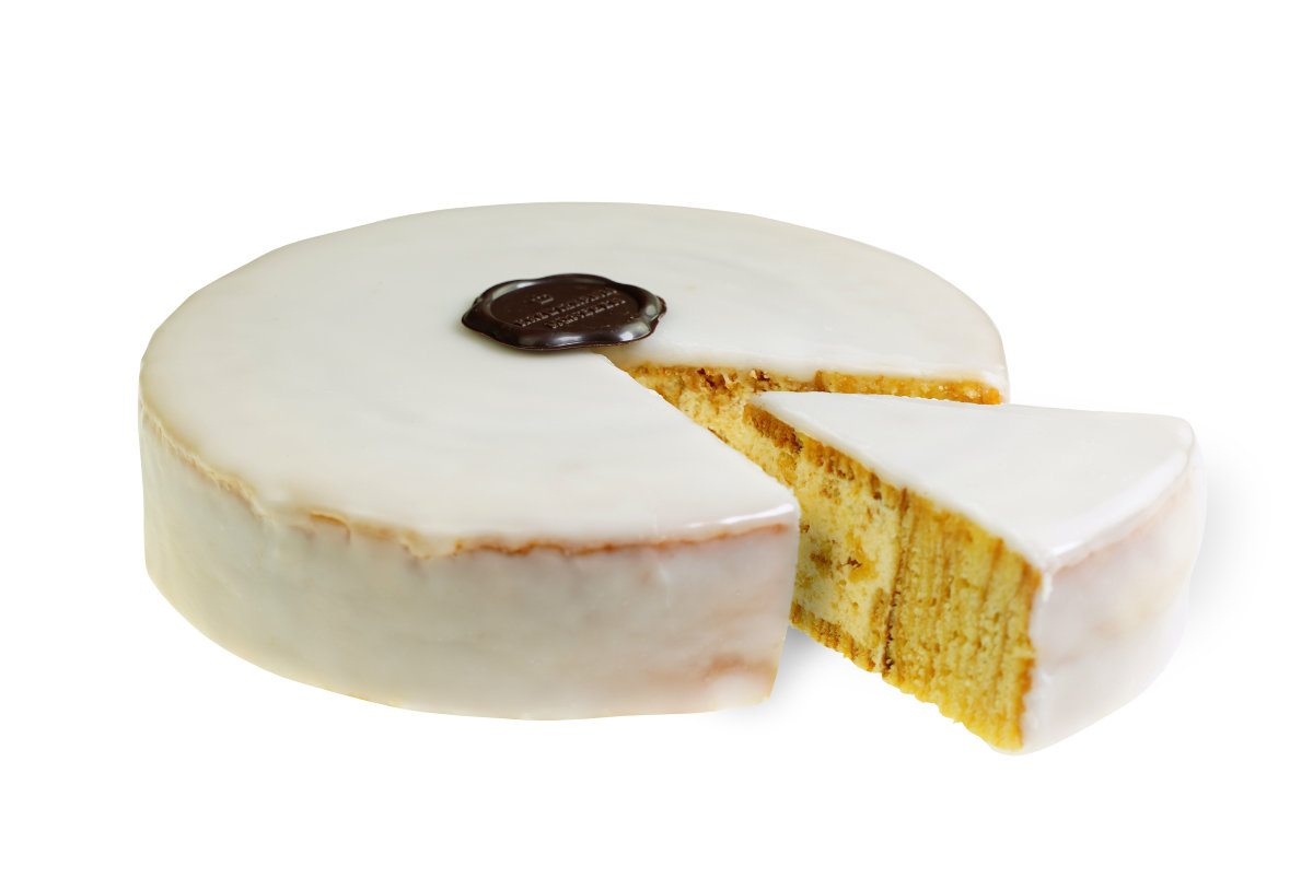 Baumkuchen-Torte-Anschnitt-Netz Kuchen-Aktion-Kontext: Rundkuchen mit weisser Glasur und Schokoladensiegel, ein Stueck herausgeschnitten, vor weissem Hintergrund. Siegeltext: "Backhaus Kreutzkamm".