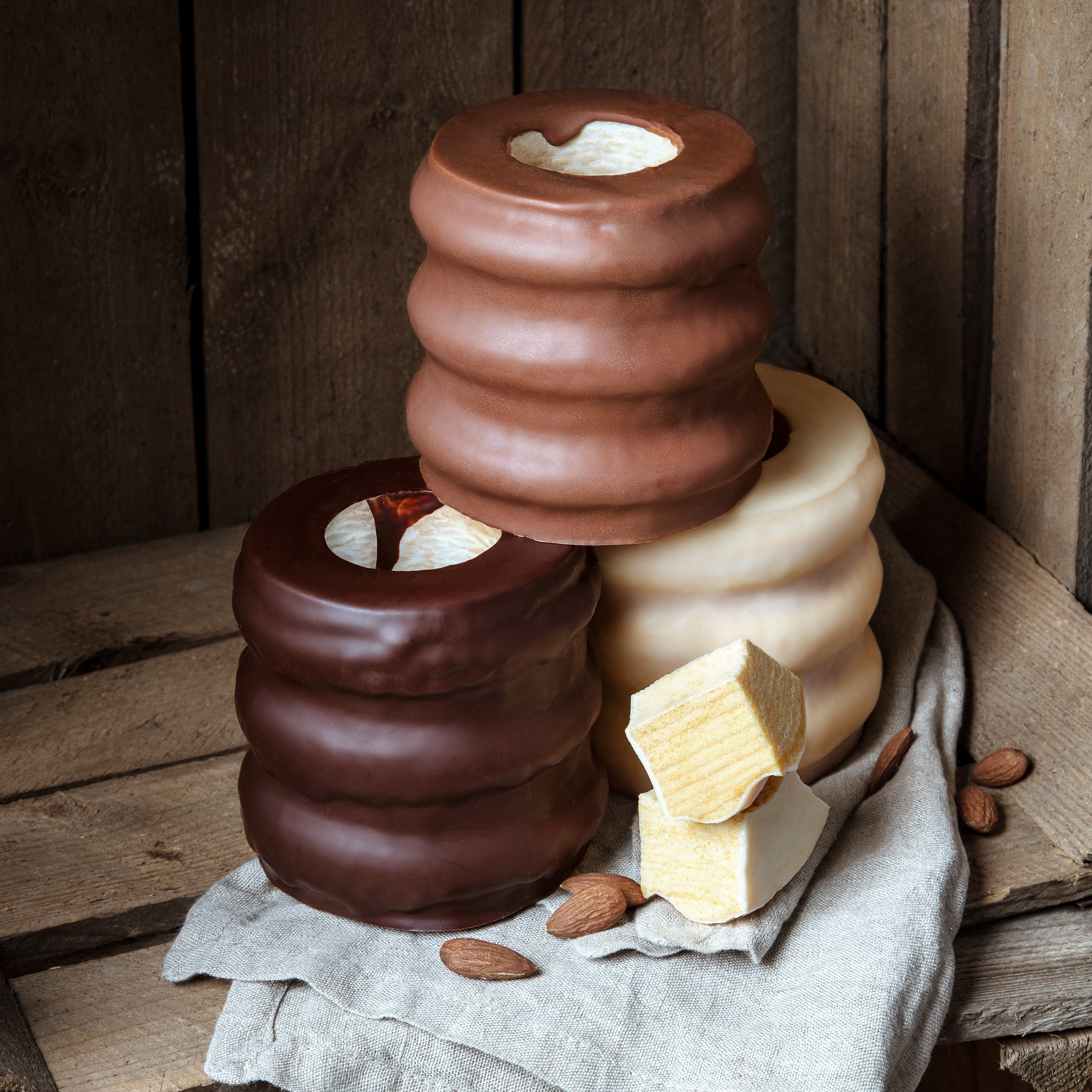 Baumkuchen_1_Post Schokoladenueberzogene Baumkuchen-Ringe, aufeinander gestapelt, auf einem rustikalen Holztisch mit Mandeln.