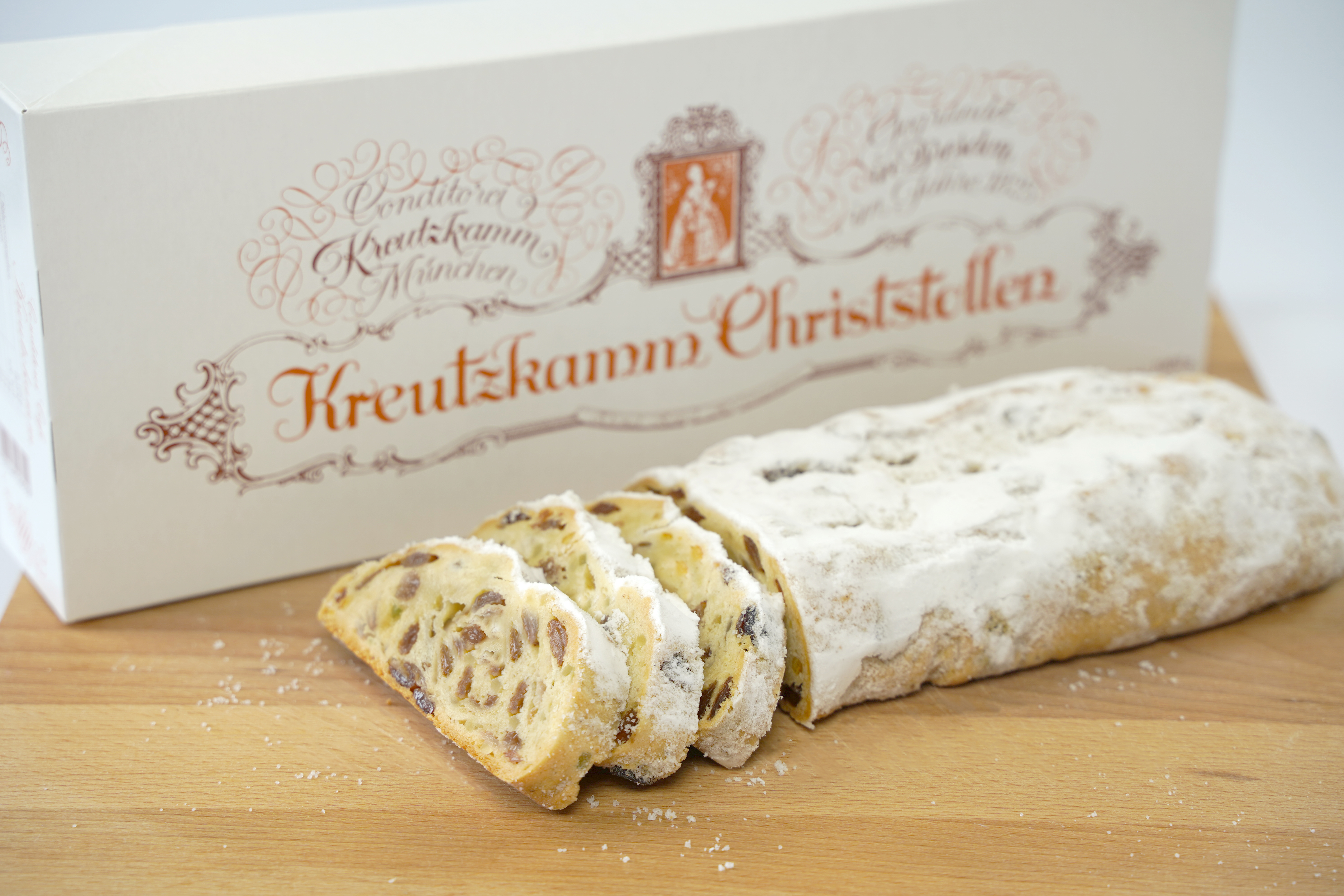 Aufgeschnittenes Christstollenbrot liegt auf einem Schneidebrett. Im Hintergrund ist eine weisse Verpackung mit der Aufschrift "Kreutzkamm Christstollen" zu sehen.