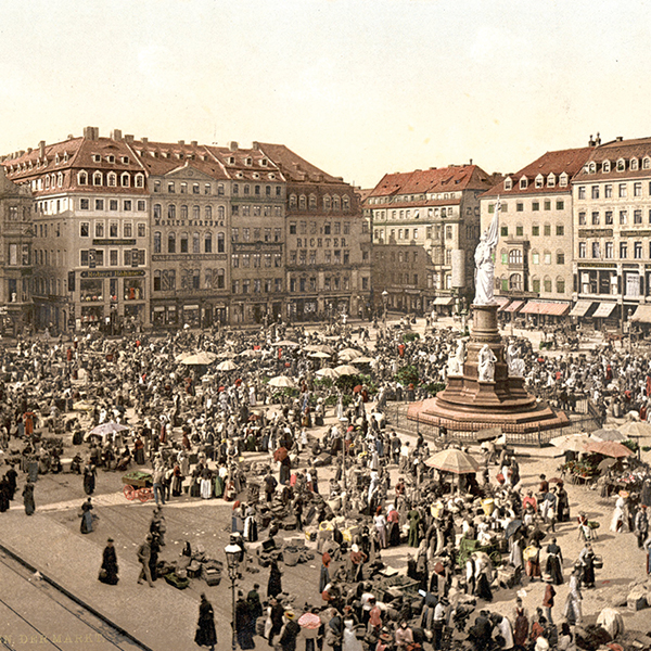 Eine belebte Menschenmenge versammelt sich auf einem grossen Marktplatz um einen Brunnen, umgeben von historischen Gebaeuden mit der Aufschrift "RICHTER ECHT."