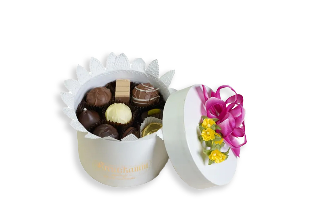 Eine geoeffnete, weisse Schachtel mit Pralinen, pinker Schleife und gelben Blumen. Text: "Kreutzkamm".